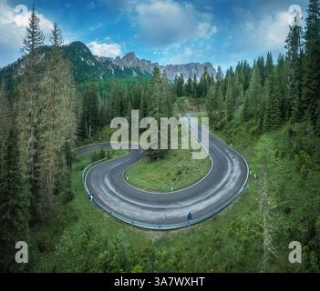 Luftaufnahme der kurvigen Straße und des grünen Waldes in den alpinen Bergen im Sommer. Dolomiten, Italien. Blick von oben auf die gewundene Straße am Bergpass, Bäume im Frühling Stockfoto