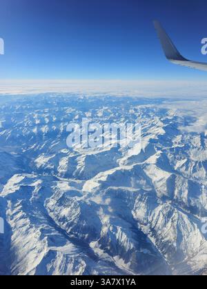Luftaufnahme des Flugzeugflügels, der über die schneebedeckten alpen fliegt Stockfoto