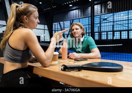 Junge Erwachsene diskutieren mit Schlägern und Getränken über Padel-Strategie am Hof Stockfoto