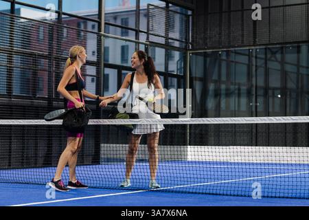 Zwei Frauen schütteln sich nach dem Freundschaftsspiel die Hände auf dem Padel-Platz und lächeln warm Stockfoto