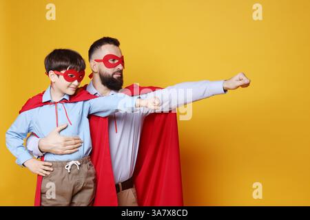 Vater und Sohn tragen Superheldenkostüme auf orangem Hintergrund Stockfoto