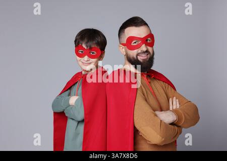 Vater und Sohn tragen Superheldenkostüme auf grauem Hintergrund Stockfoto