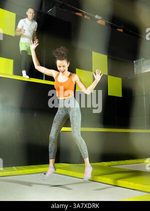 Glückliche Frau mittleren Alters, die auf Trampolinen in einem Sporthalle trampoliniert und springt, Workout und modernes Unterhaltungskonzept Stockfoto