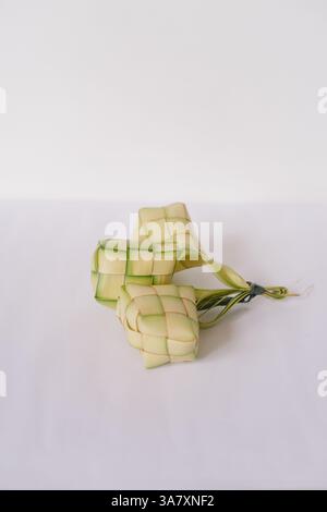 Ketupat, ein traditioneller südostasiatischer Reisknödel, präsentiert auf einem sauberen weißen Hintergrund. Die gewebten Palmblattbeutel und ihr einzigartiges Muster Stockfoto