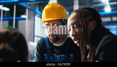 Der Leiter der Photovoltaik-Fabrik gibt den Arbeitern Aufgaben und fordert sie auf, die Systemparameter anzupassen. Teamleiter erklärt den Mitarbeitern, wie die Energieversorgung in der Solarpaneelfertigungsanlage, Kamera B, optimiert werden kann Stockfoto