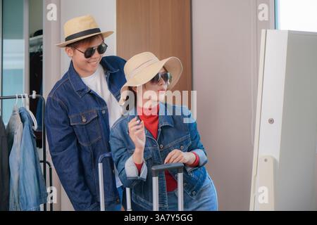 Junge Männer und Frauen stehen vor einem Spiegel, sowohl in Jeansjacken als auch in stylischen Sonnenbrillen. Umgeben von Hüten und einem Kleiderständer, strahlen sie Betrüger aus Stockfoto