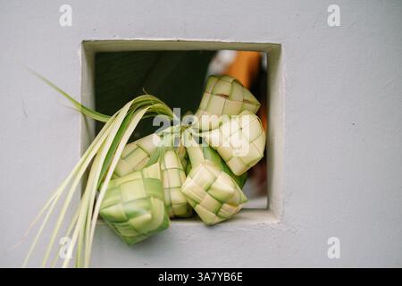 Nahaufnahme von Ketupat, einem traditionellen Reisknödel aus Südostasien, der während der Eid al-Fitr-Feier an einem Fenster hängt. Die rautenförmige Stockfoto