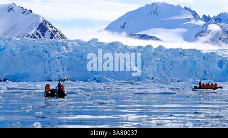 Arktische Landschaft mit Touristen auf Booten vor der Kulisse eines Gletschers und schneebedeckter Berge im Krossfjord im Svalbard-Archipel Stockfoto