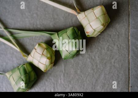 Ein Bild von sorgfältig gewebtem Ketupat, einem traditionellen Reisknödel, auf einem strukturierten Hintergrund. Diese blattgewickelten Blätter repräsentieren das kulinarische Erbe Stockfoto