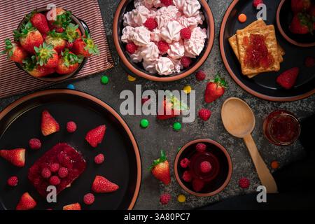 Blick von oben auf Desserts, Süßigkeiten, Marmelade und Erdbeermarmelade auf einem schwarzen Keramiktisch mit Erdbeeren Stockfoto