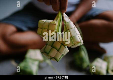 Nahaufnahme von jemandem, der frisch zubereitetes Ketupat hält, ein traditionelles Gericht aus Reis, verpackt in einem gewebten Palmblattbeutel. Dieses Gericht ist beliebt bei mir Stockfoto