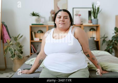 Porträt einer Frau, die auf dem Bett im friedlichen Raum sitzt Stockfoto