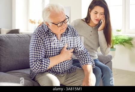 Die junge Tochter ruft den Notfall an, um ihrem älteren Vater zu helfen, der einen Herzinfarkt hat Stockfoto