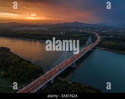 Budapest, Ungarn - aus der Vogelperspektive auf die Megyeri-Brücke über die Donau in der Abenddämmerung mit einem wunderschönen dramatischen goldenen Sonnenuntergang und den Buda-Hügeln Stockfoto