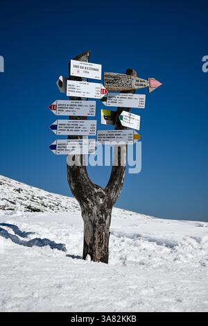 Hölzerne Wegweiser mit verschiedenen Zielen und Entfernungen in einem schneebedeckten Berg an einem sonnigen Tag. Stockfoto