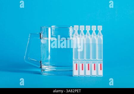 Eine Tasse Wasser und Röhrchen mit einer neuen Generation von Metabiotika auf blauem Hintergrund. Darmbehandlung, Wiederherstellung der Mikroflora nach Dysbacter Stockfoto