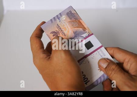 Eine Nahaufnahme zeigt, dass die Hände einer Person ein ordentlich gestapeltes Bündel indonesischer Rupiah-Banknoten handhaben. Der Schwerpunkt liegt auf der Textur und den Details von t Stockfoto