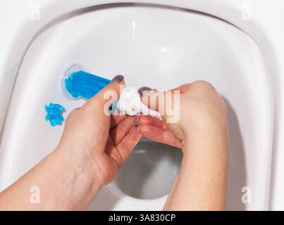 Eine Spritze mit ozeanduftendem Gel zur Reinigung und Desinfektion der Toilette in einer Hand vor dem Hintergrund einer Toilette. Antibakterielle Wirkung Stockfoto