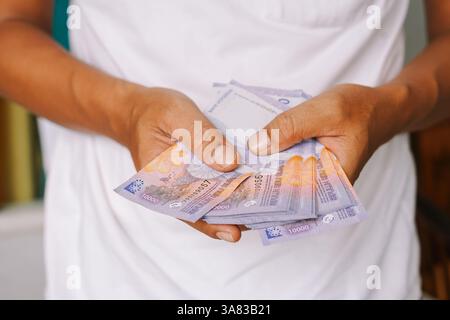 Nahaufnahme einer Person, die indonesische Rupiah-Banknoten hält. Symbolisiert finanziellen Wohlstand, Investitionsmöglichkeiten und Wirtschaftswachstum in I Stockfoto
