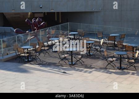 Leere Terrasse im Freien mit Bistrostühlen aus Holz und runden Tischen, umgeben von Glasbarrieren Stockfoto
