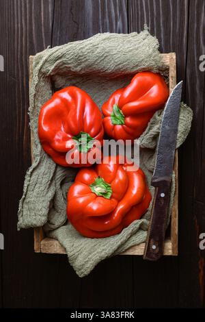 Blick von oben auf drei frische rote süße Paprika in rustikaler Holzkiste aus nächster Nähe. Ästhetische Lebensmittelfotografie Stockfoto