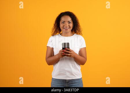 Lächelnde junge afroamerikanische Frau, die ihr Smartphone beiläufig benutzt Stockfoto