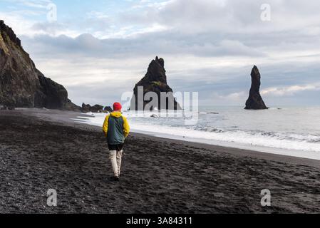 Man spaziert entlang des malerischen schwarzen Sandstrands von Reynisfjara, Island Stockfoto