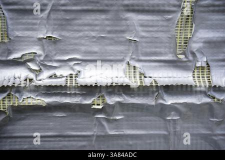 Ein beschädigtes Dach mit gerissenen Schindeln und freiliegender Dämmung, was darauf hinweist, dass aufgrund von Witterungseinflüssen eine Reparatur erforderlich ist. Hochwertige Fotos Stockfoto