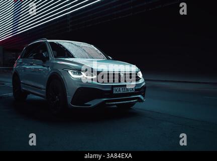 Volkswagen Tiguan nachts auf der dunklen Stadtstraße. Vorderansicht des modernen SUV bei Nacht mit leuchtenden LED-Linien über dem Hintergrund. Stockfoto