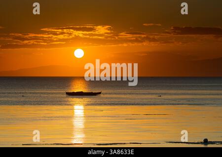 Ein friedlicher Sonnenuntergang wirft goldenes Licht über ein ruhiges Meer, und die Silhouette eines einsamen Bootes verleiht der malerischen Aussicht Tiefe und ruft Ruhe hervor Stockfoto