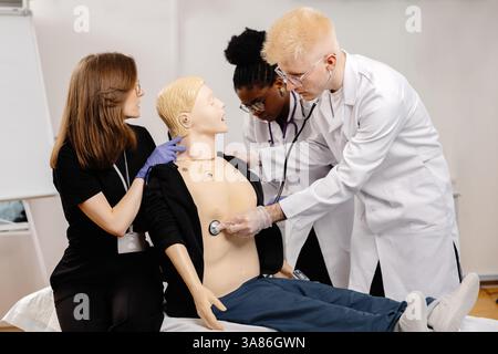 Gruppe verschiedener Medizinstudierenden, die sich mit dem Stethoskop anatomisches Modell während der Praxissitzung untersuchen Stockfoto