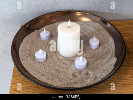 Elektrische LED-Kerzen in Sand in einer großen Schüssel. Innenraum. Stockfoto