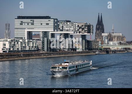 Köln, Deutschland. März 2025. Ein Passagierschiff überquert bei sonnigem Wetter den Rhein am Dom (r) und den Kranhäusern (l) am Rheinauhafen. Quelle: Oliver Berg/dpa/Alamy Live News Stockfoto