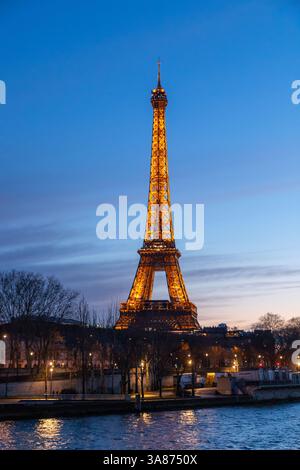 Paris, Frankreich - 24. Februar 2025: Nächtlicher Blick auf den beleuchteten Eiffelturm an der seine in Paris, Frankreich. Vertikales Foto Stockfoto
