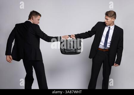 Wettbewerbskonzept. Geschäftsleute ziehen Lederaktentasche auf grauem Hintergrund Stockfoto