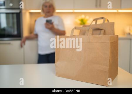 Seniorin, die Lebensmittel erhält, Einkaufstaschen auf dem Tisch in der Küche Stockfoto