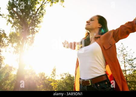Flacher Blick auf die Frau, die die Natur mit ausgestreckten Armen in friedlicher Umgebung im Freien umgibt. Stockfoto