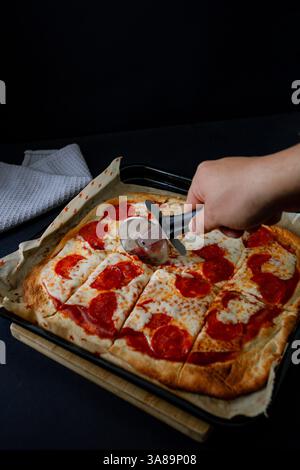 Gourmet-Pepperoni-Pizza im dunklen Stil, die ihre Zutaten in einem raffinierten Ambiente hervorhebt. Stockfoto