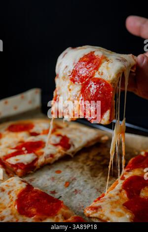 Gourmet-Pepperoni-Pizza im dunklen Stil, die ihre Zutaten in einem raffinierten Ambiente hervorhebt. Stockfoto