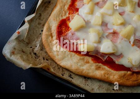 Hawaiianische Gourmet-Pizza im dunklen Stil, die ihre Zutaten in einem raffinierten Ambiente hervorhebt. Stockfoto