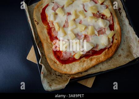 Hawaiianische Gourmet-Pizza im dunklen Stil, die ihre Zutaten in einem raffinierten Ambiente hervorhebt. Stockfoto