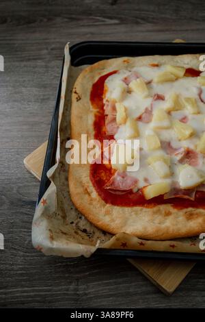 Hawaiianische Gourmet-Pizza im dunklen Stil, die ihre Zutaten in einem raffinierten Ambiente hervorhebt. Stockfoto