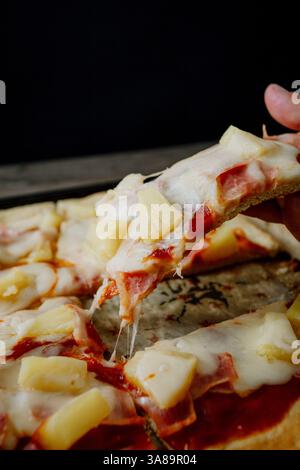 Hawaiianische Gourmet-Pizza im dunklen Stil, die ihre Zutaten in einem raffinierten Ambiente hervorhebt. Stockfoto