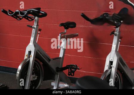 Zwei Indoor-Radfahrräder, die in einem Fitnessstudio an einer roten Wand angebracht sind. Stockfoto