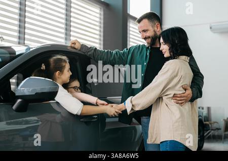 Eine glückliche junge Familie in einem modernen Autohaus nach dem Kauf eines neuen Familienautos. Das Konzept des Mietens, Testfahrens eines Autos. Stockfoto