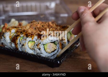 Personen nehmen knuspriges Drachenrollen-Sushi mit Essstäbchen aus dem Take Out-Behälter Stockfoto