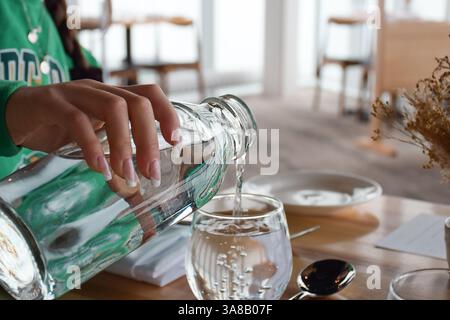 Junge Frau, die Wasser aus der Flasche ins Glas im Restaurant gießt Stockfoto