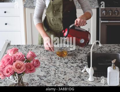 Frau gießt heißes Wasser in eine Tasse, um Tee in der Küche zu machen Stockfoto