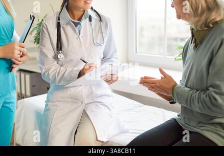 Ärztin sitzt in der Nähe eines älteren Patienten, schreibt auf das Klemmbrett, gibt Gesundheitsberatung in der Klinik. Stockfoto