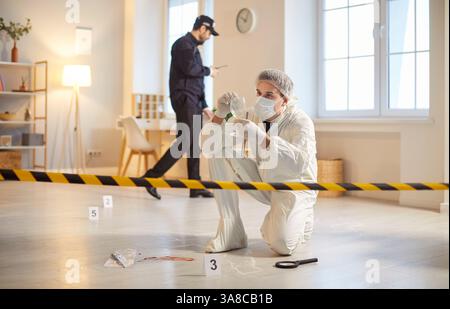 Fokussierter forensischer Experte untersucht Beweise am Tatort, während Polizist in der Nähe arbeitet. Stockfoto